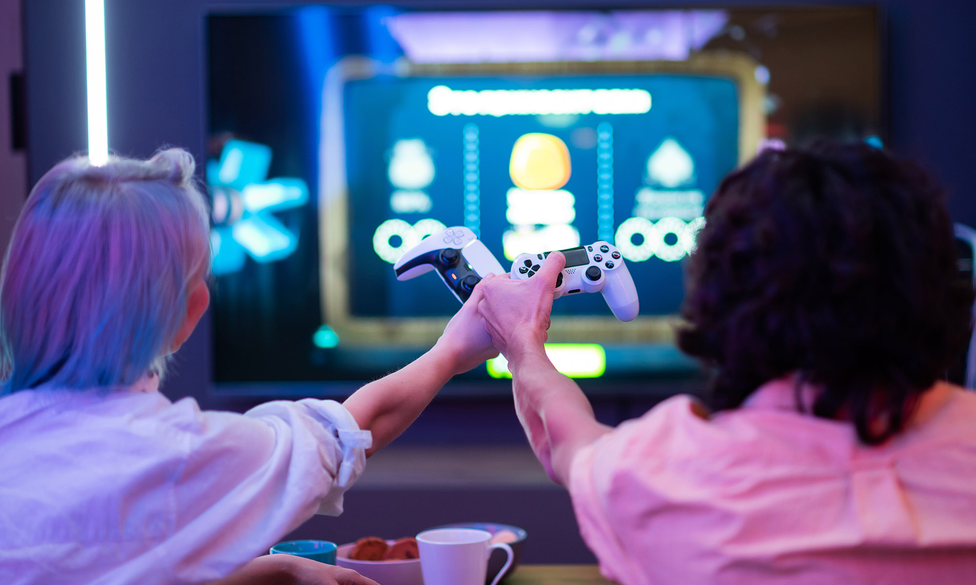 Two positive person guy and lady sitting on sofa having fun playing video games celebrating win raising hands up in colorful interior room ady sitting on sofa