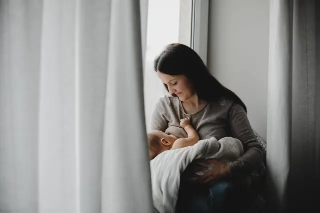 Mother holds newborn boy her arms while she feeds him scaled